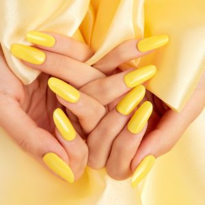 A closeup shot of a female's hands with yellow nail polish on a yellow silk fabric