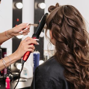 hands of a hairdresser with a Curling iron making a hairstyle for a curly girl in a professional beauty salon