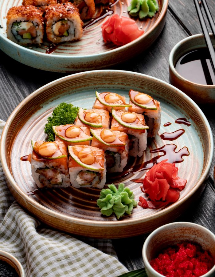 side view of sushi rolls with shrimps avocado and cream cheese served with ginger and wasabi on a plate on wooden background